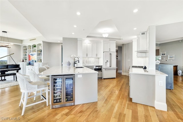 kitchen with high end white refrigerator, sink, decorative light fixtures, beverage cooler, and light hardwood / wood-style floors