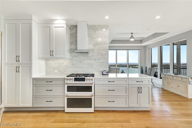 4931 Bonita Bay Blvd Unit 2103, Bonita Springs, FL 34134 - kitchen featuring range with two ovens, wall chimney range hood, a ceiling fan, a tray ceiling, and decorative backsplash
