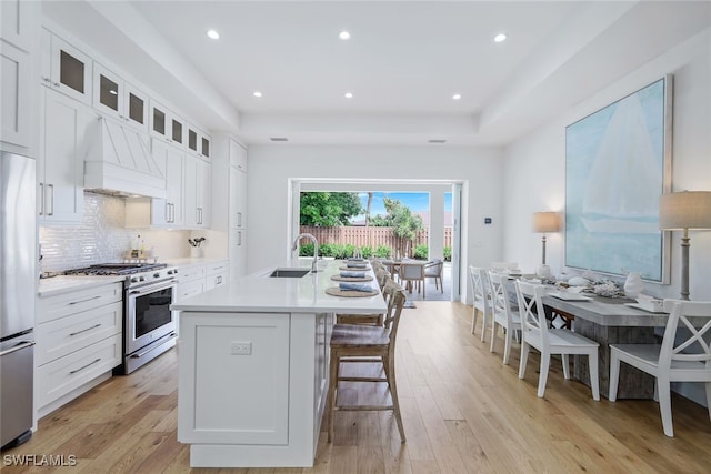 kitchen with stainless steel appliances, premium range hood, sink, and white cabinetry