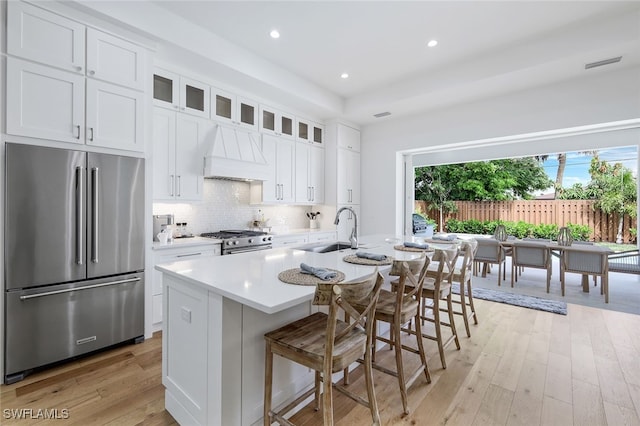 kitchen featuring white cabinetry, sink, premium appliances, custom range hood, and a center island with sink