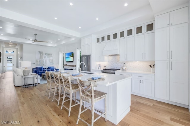 kitchen featuring custom exhaust hood, white cabinetry, a breakfast bar area, and a large island with sink