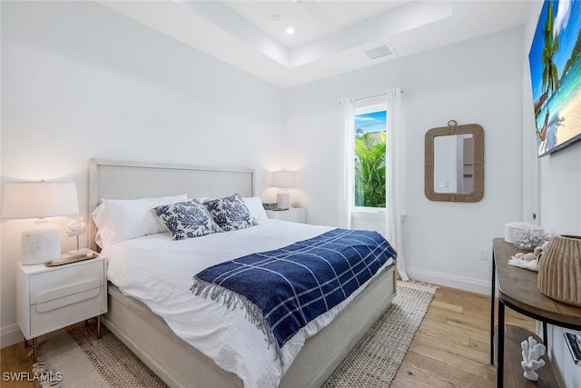 bedroom with a tray ceiling and light hardwood / wood-style flooring