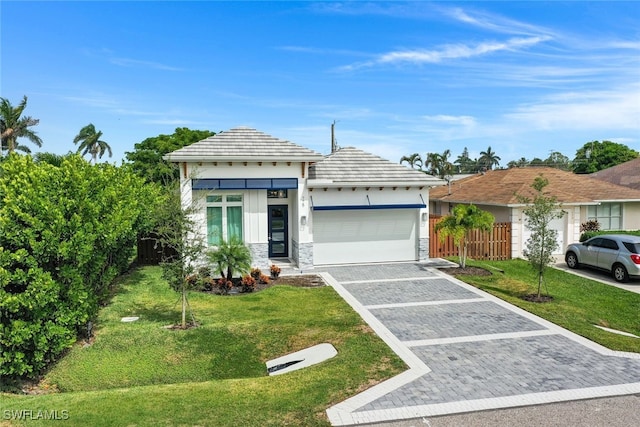 view of front of house featuring an attached garage, fence, stone siding, decorative driveway, and a front lawn