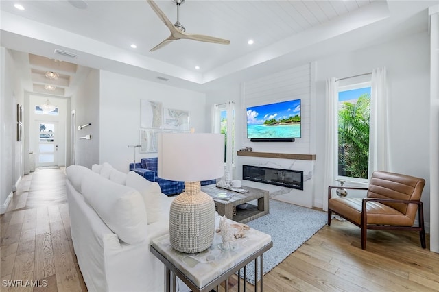 living room with a premium fireplace, a raised ceiling, and light hardwood / wood-style flooring