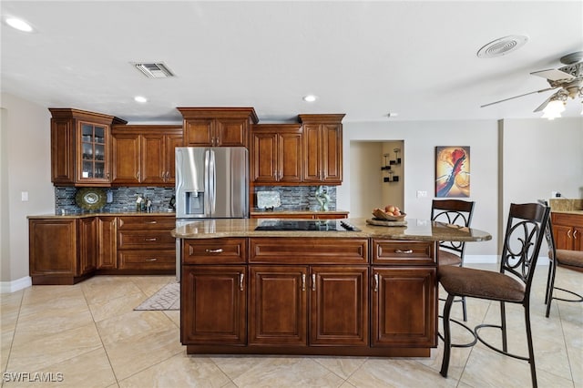 kitchen with tasteful backsplash, stainless steel refrigerator with ice dispenser, a kitchen island, and light stone counters