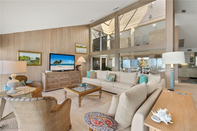 living room featuring wood walls, a skylight, high vaulted ceiling, and light wood-type flooring