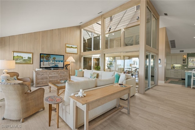 living room with light hardwood / wood-style flooring, plenty of natural light, high vaulted ceiling, and wood walls