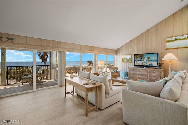 living room featuring lofted ceiling, light hardwood / wood-style flooring, wooden walls, and a water view