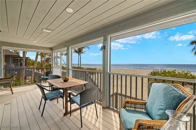 sunroom / solarium featuring a water view, wooden ceiling, and a view of the beach