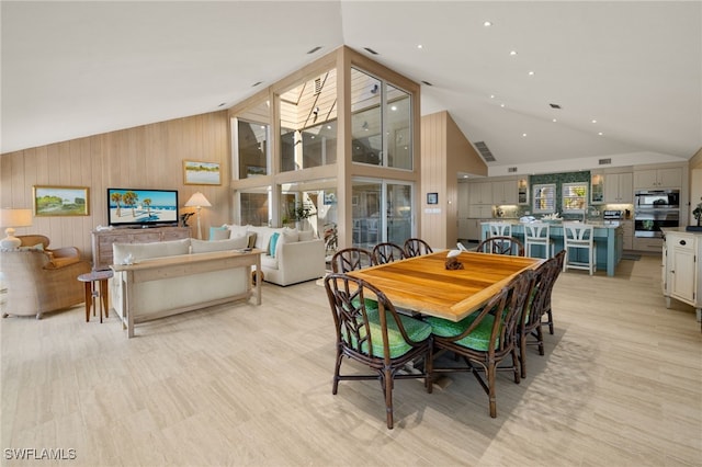 dining area featuring high vaulted ceiling, wooden walls, and light hardwood / wood-style floors