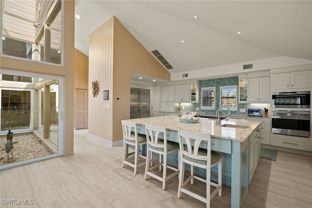 kitchen with an island with sink, sink, a kitchen bar, stainless steel appliances, and light stone countertops