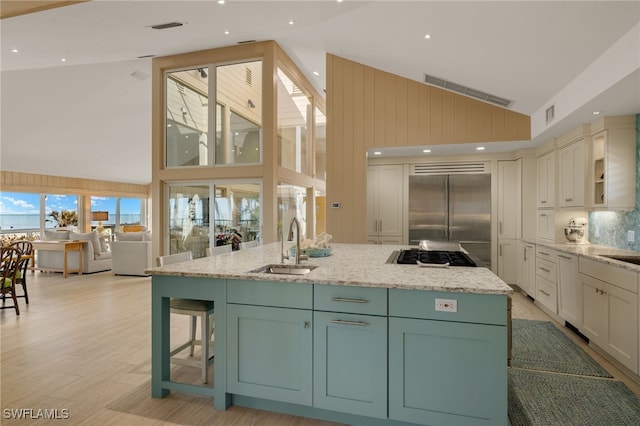 kitchen with sink, a kitchen island with sink, stainless steel appliances, a kitchen breakfast bar, and light stone counters