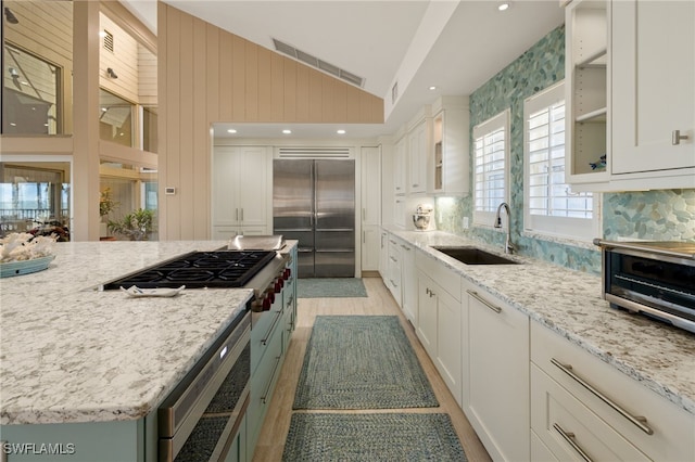 kitchen with sink, white cabinetry, light stone counters, vaulted ceiling, and stainless steel appliances