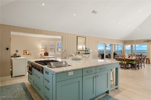 kitchen featuring a water view, light stone counters, appliances with stainless steel finishes, a kitchen island with sink, and light hardwood / wood-style floors