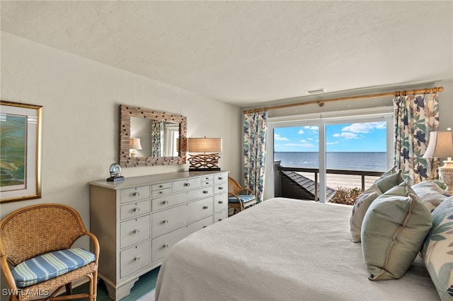 bedroom featuring access to exterior, a textured ceiling, and a water view