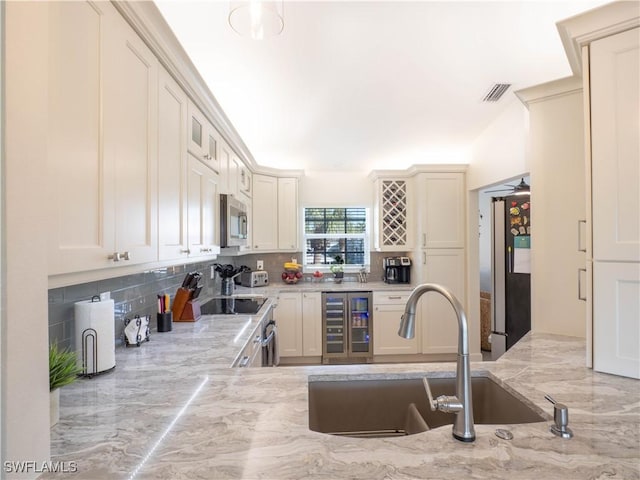 kitchen with wine cooler, sink, black fridge, light stone counters, and decorative backsplash