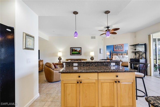 kitchen featuring light tile patterned floors, ceiling fan, a kitchen breakfast bar, a kitchen island, and dark stone counters