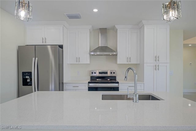 kitchen featuring wall chimney exhaust hood, appliances with stainless steel finishes, hanging light fixtures, and light stone countertops