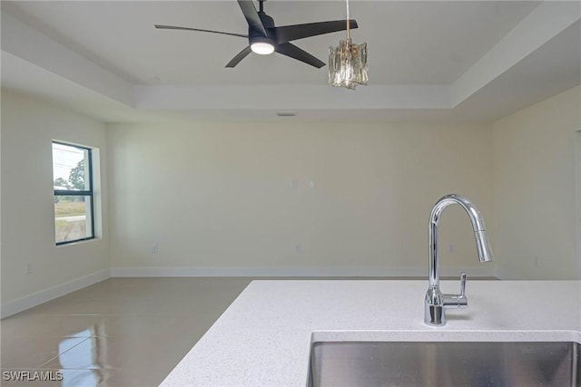 interior space with baseboards, tile patterned floors, a tray ceiling, light countertops, and a sink