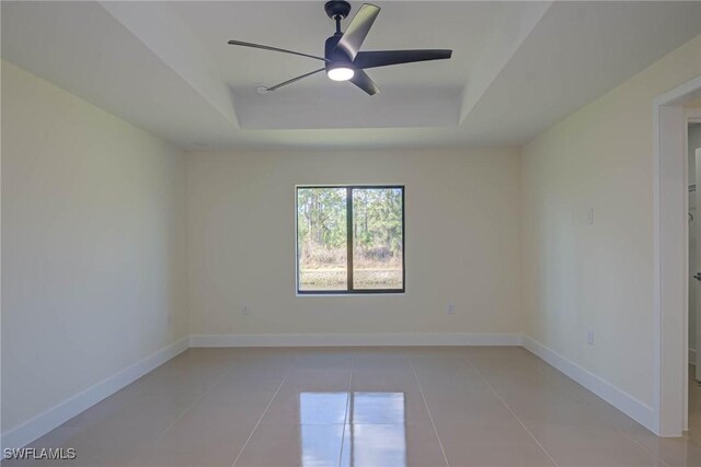 spare room featuring ceiling fan, light tile patterned floors, a raised ceiling, and baseboards