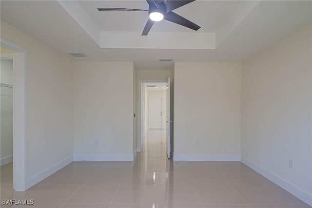 spare room featuring light tile patterned floors, baseboards, a tray ceiling, and a ceiling fan