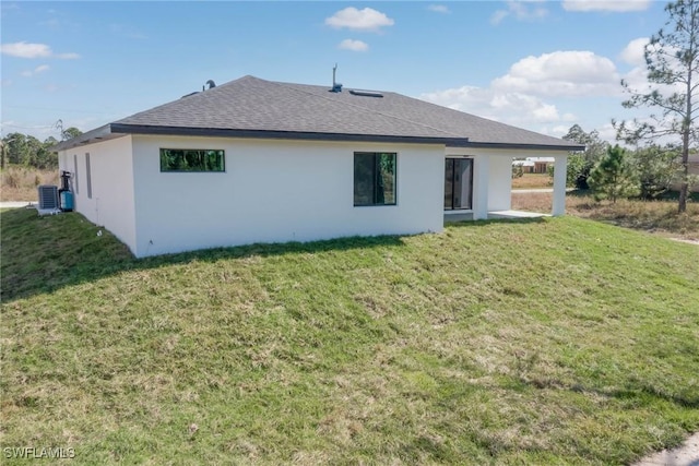 rear view of property featuring roof with shingles, a lawn, stucco siding, and central air condition unit