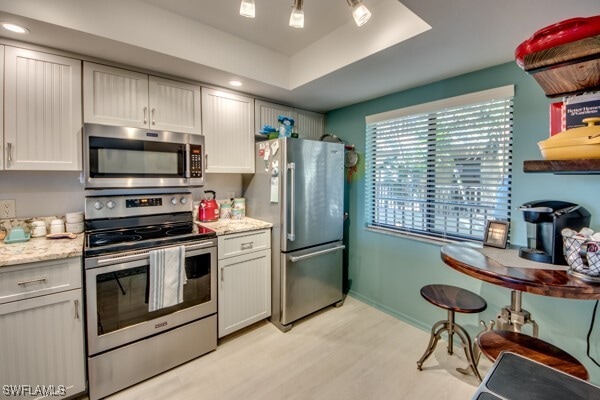 kitchen with a raised ceiling, white cabinetry, light stone counters, light hardwood / wood-style floors, and stainless steel appliances