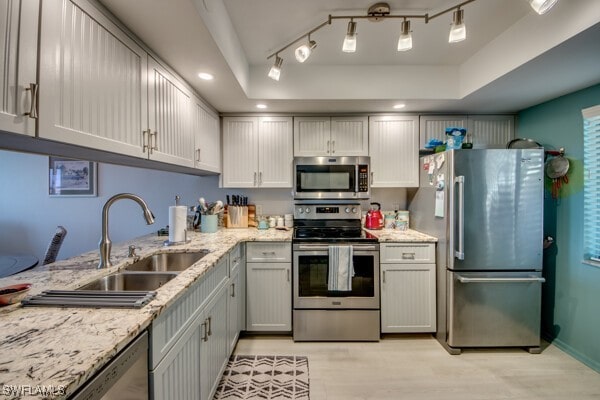 kitchen with a tray ceiling, stainless steel appliances, recessed lighting, a sink, and light stone countertops