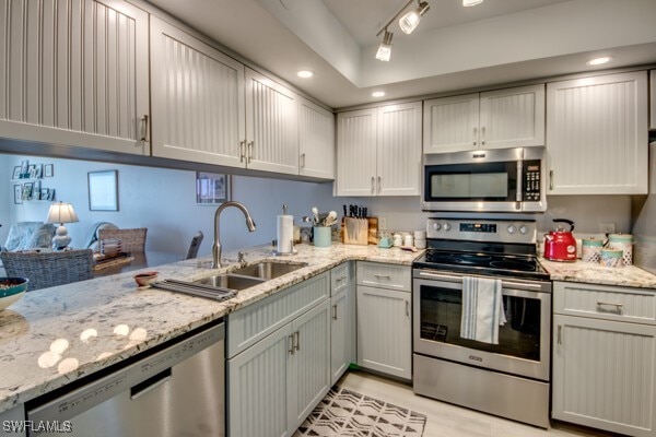 kitchen with appliances with stainless steel finishes, a sink, light stone counters, and recessed lighting