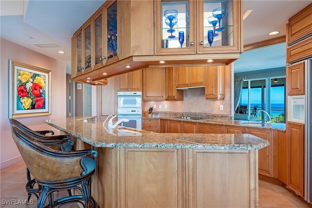 kitchen featuring sink, light tile patterned floors, black electric cooktop, and a breakfast bar