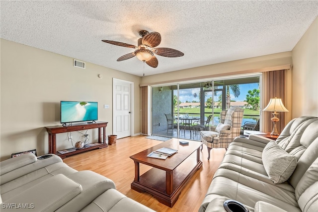 living room featuring ceiling fan, light hardwood / wood-style flooring, and a textured ceiling