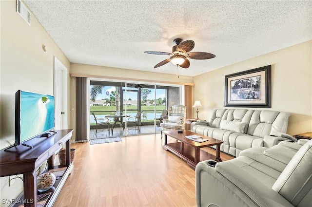 living room with ceiling fan, a textured ceiling, and light wood-type flooring