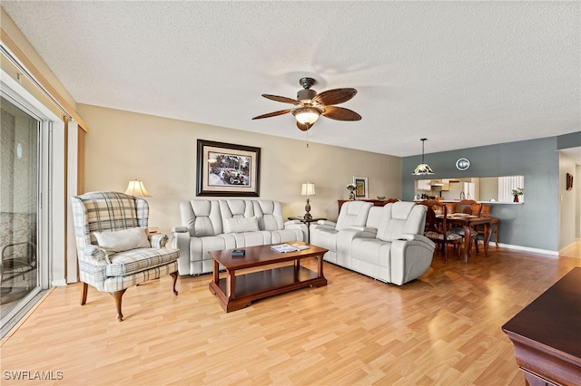 living room featuring ceiling fan, light hardwood / wood-style flooring, and a textured ceiling