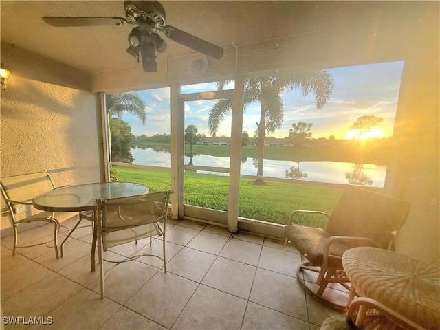 sunroom with ceiling fan and a water view