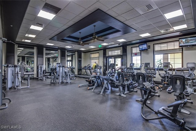 exercise room with ceiling fan, a paneled ceiling, and a raised ceiling