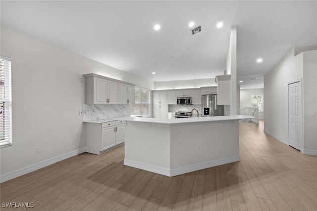 kitchen with lofted ceiling, tasteful backsplash, a center island, appliances with stainless steel finishes, and light hardwood / wood-style floors