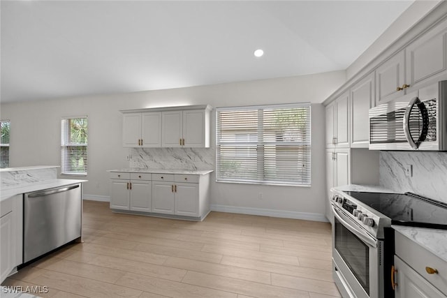 kitchen with vaulted ceiling, appliances with stainless steel finishes, tasteful backsplash, white cabinets, and light stone countertops