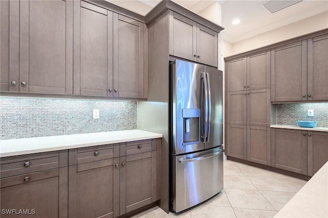 kitchen with tasteful backsplash, light tile patterned floors, ornamental molding, and stainless steel refrigerator with ice dispenser