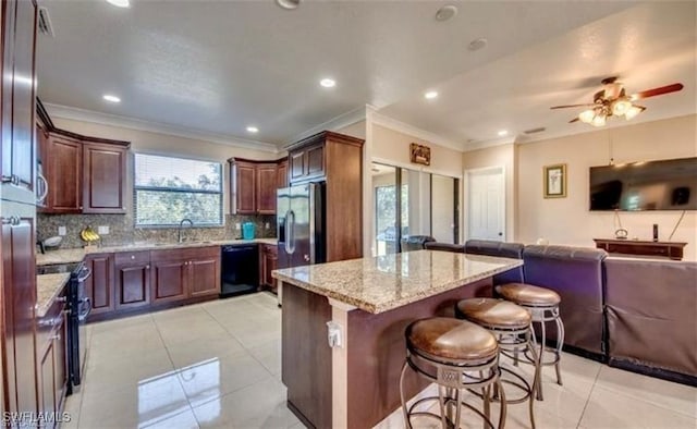 kitchen featuring backsplash, a center island, light stone counters, black appliances, and a kitchen bar