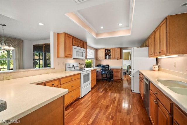 kitchen with wood-type flooring, sink, hanging light fixtures, a tray ceiling, and white appliances