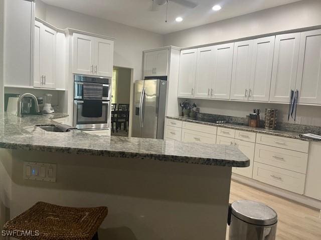 kitchen with white cabinetry, appliances with stainless steel finishes, kitchen peninsula, and dark stone counters