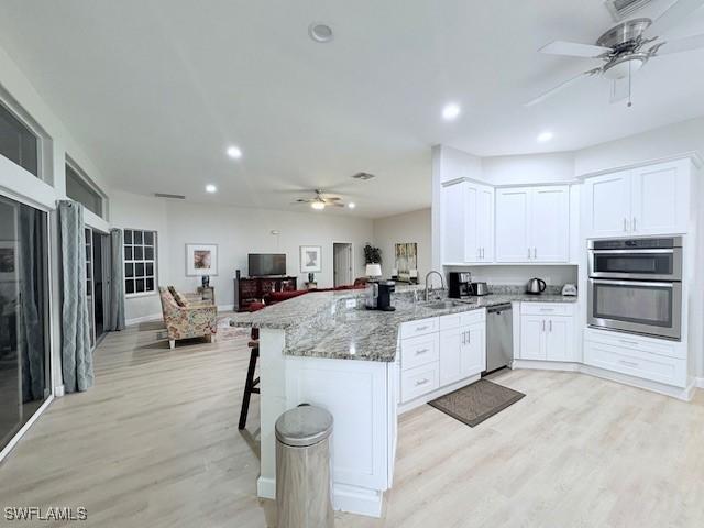 kitchen featuring appliances with stainless steel finishes, a kitchen breakfast bar, light stone countertops, white cabinets, and kitchen peninsula