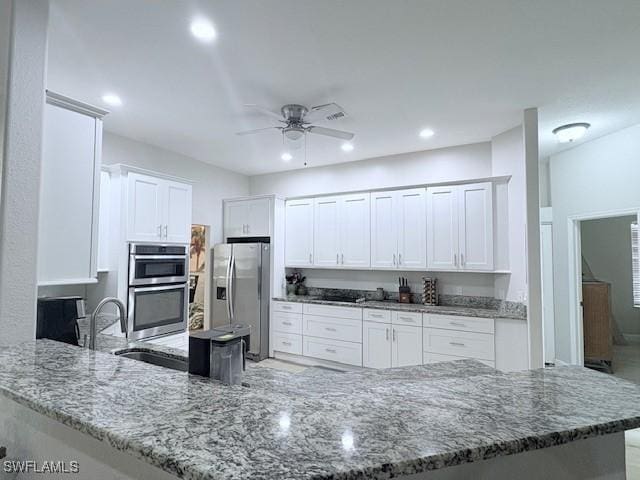 kitchen with stainless steel appliances, white cabinetry, stone countertops, and kitchen peninsula