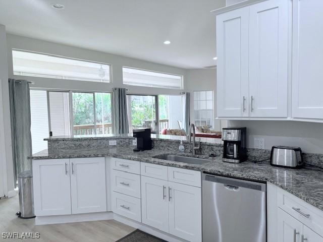 kitchen featuring dishwasher, sink, white cabinets, dark stone counters, and light hardwood / wood-style flooring