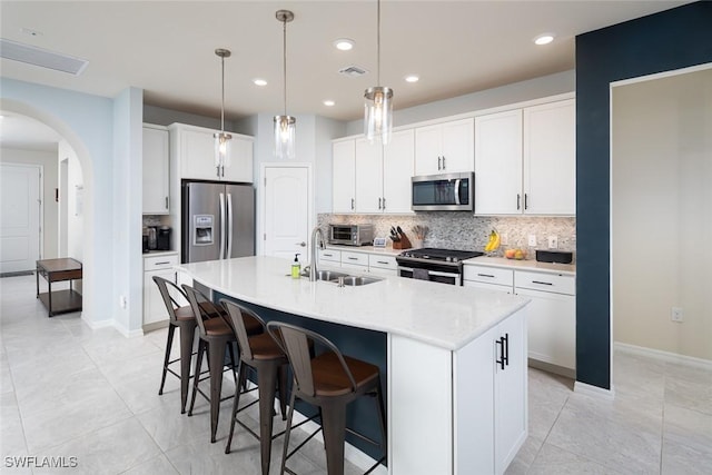 kitchen featuring hanging light fixtures, white cabinetry, appliances with stainless steel finishes, and a center island with sink