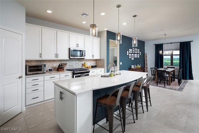 kitchen featuring sink, white cabinetry, a center island with sink, appliances with stainless steel finishes, and pendant lighting