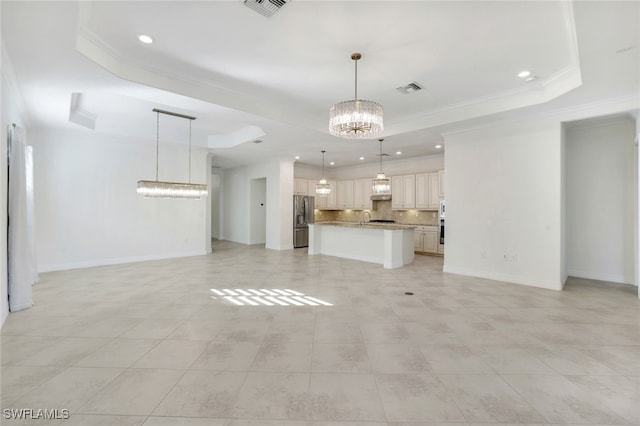 unfurnished living room featuring a notable chandelier, a tray ceiling, ornamental molding, and sink