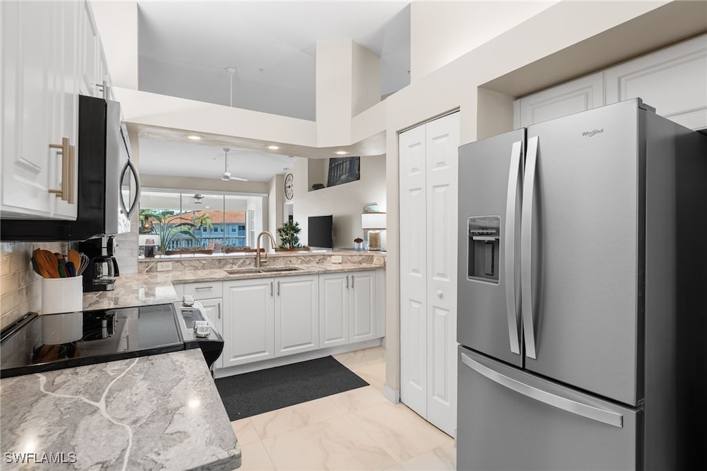 kitchen with sink, appliances with stainless steel finishes, white cabinetry, a high ceiling, and light stone countertops