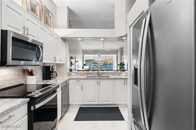 kitchen with sink, appliances with stainless steel finishes, white cabinetry, backsplash, and light stone counters