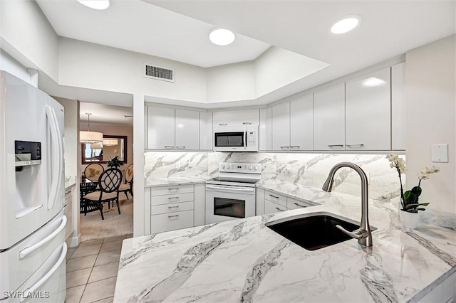 kitchen featuring sink, white appliances, white cabinetry, backsplash, and light stone countertops